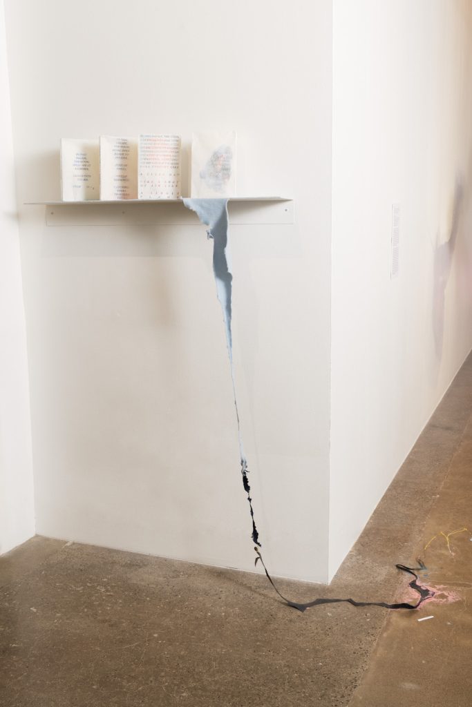 4 tablets made of rice paper with text on them, sitting on white shelf on white wall. A soft blue fleece goes from the shelf to the floor petering out into other materials (wool, wire...)